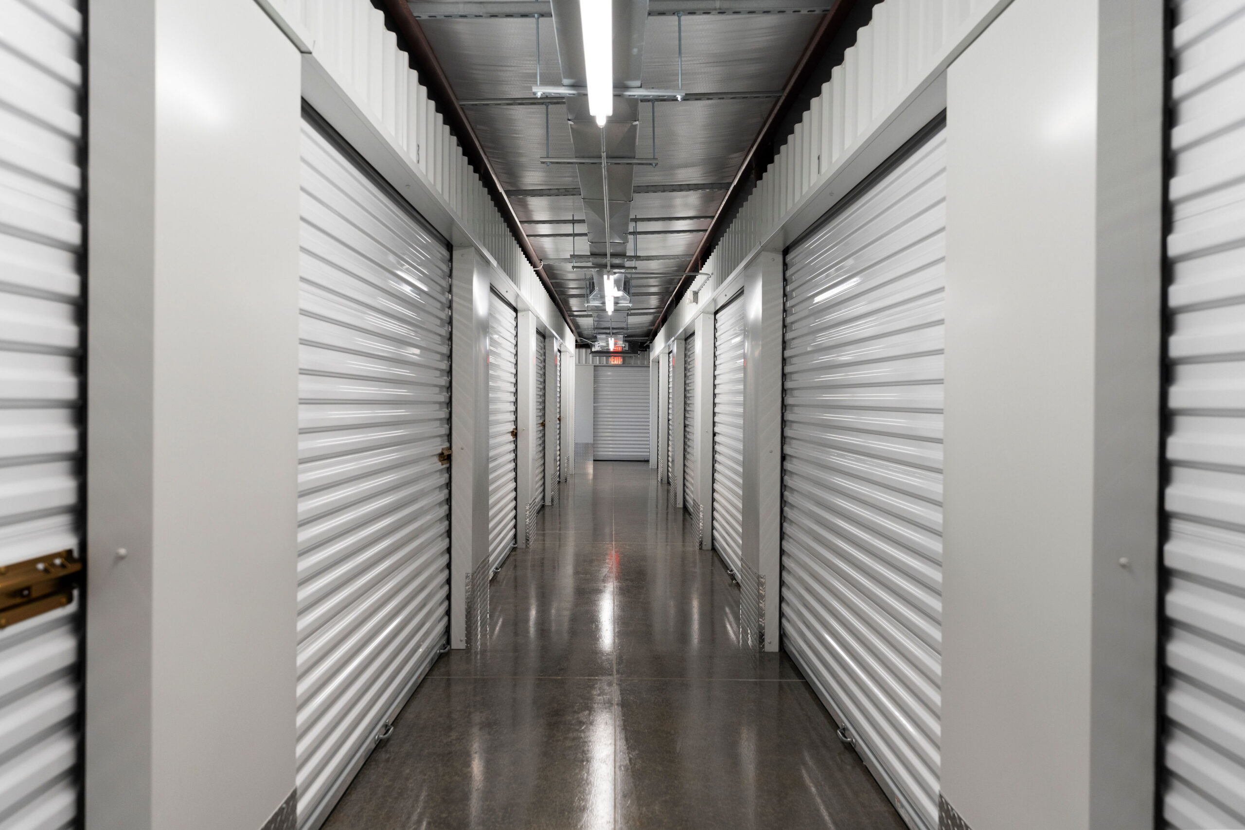 Well-lit indoor hallway lined with white roll-up unit doors